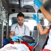 View from inside ambulance of uniformed emergency services workers caring for patient on stretcher during coronavirus pandemic. View from inside ambulance of uniformed emergency services workers caring for patient on stretcher during coronavirus pandemic.